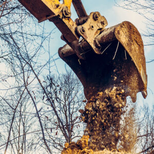 Backdrop of excavator bucket with soil on forest and sky background.2020